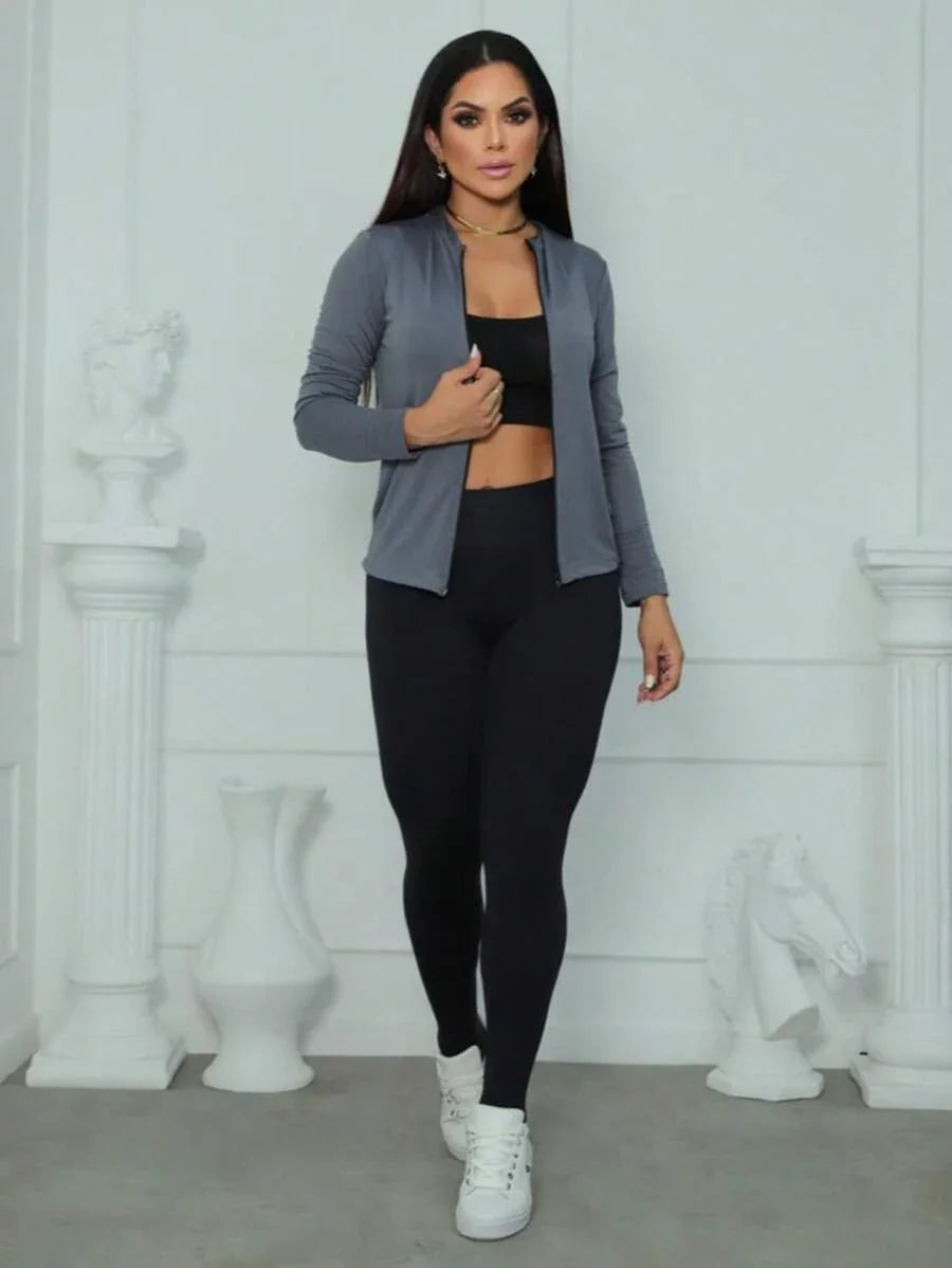 Mulher usando casaco cinza, leggings pretas e tênis branco em fundo branco fosco com esculturas clássicas