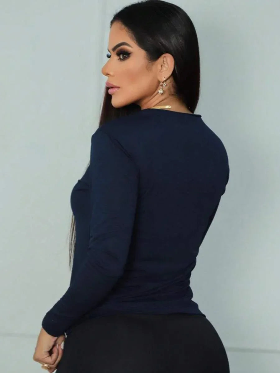 Mulher vista de costas com blusa azul escura de manga longa e calça preta, fundo branco fosco