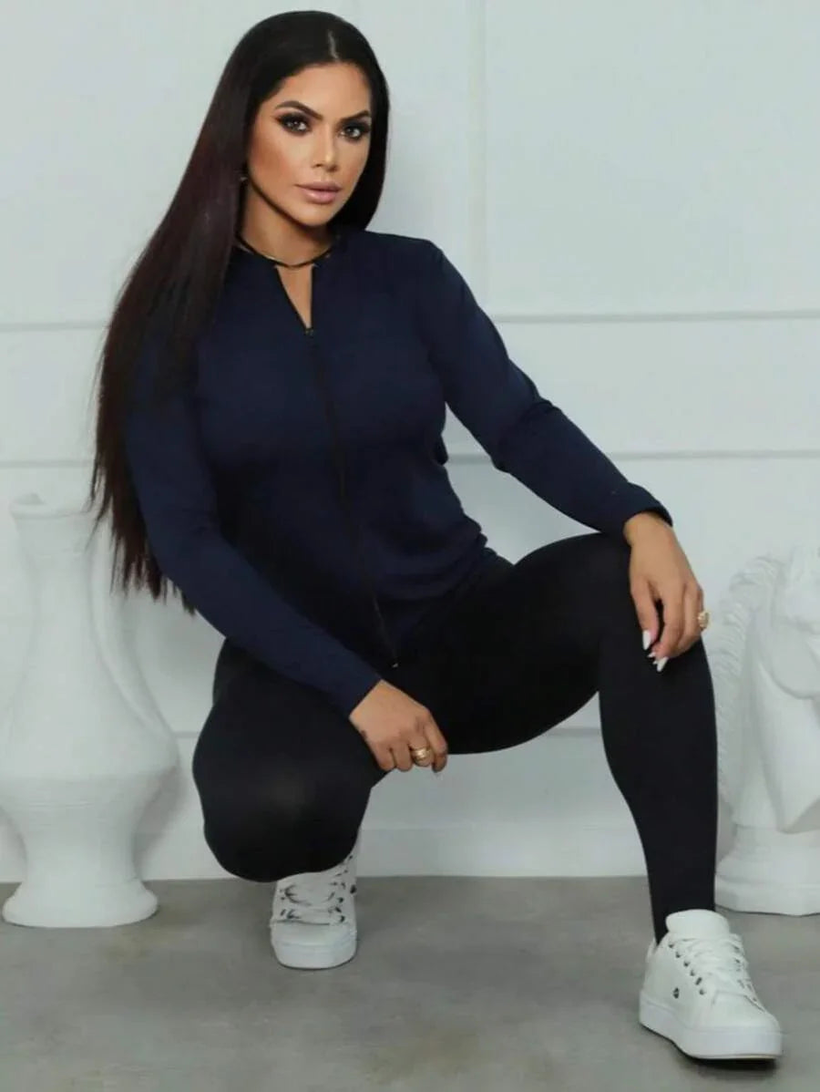 Mulher agachada com casaco azul escuro, legging preta e tênis branco em fundo branco fosco