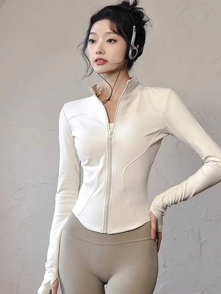 Mulher vestindo jaqueta branca esportiva com zíper e calça legging bege, fundo branco fosco